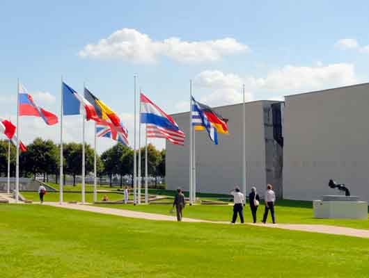 Vue ensoleillée de l'entrée du Mémorial de Caen et ses drapeaux